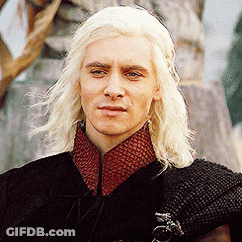 A Man With Blonde Hair Is Wearing A Black Cape And Red Collar GIF