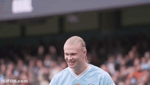 A Man With Blonde Hair Is Wearing A Blue Shirt And Smiling On A Soccer Field . GIF
