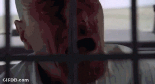 A Man With Blood On His Face Is Behind Bars In A Cell . GIF