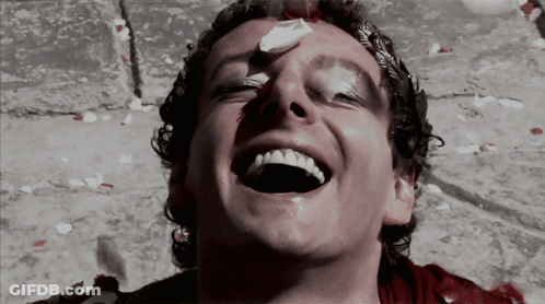 A Man With Blood On His Face Is Laughing With Petals Falling Around Him GIF