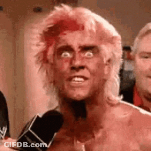 A Man With Blood On His Face Is Talking Into A Microphone While Wearing A Mullet . GIF