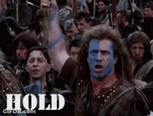 A Man With Blue And White Paint On His Face Is Standing In Front Of A Crowd . GIF