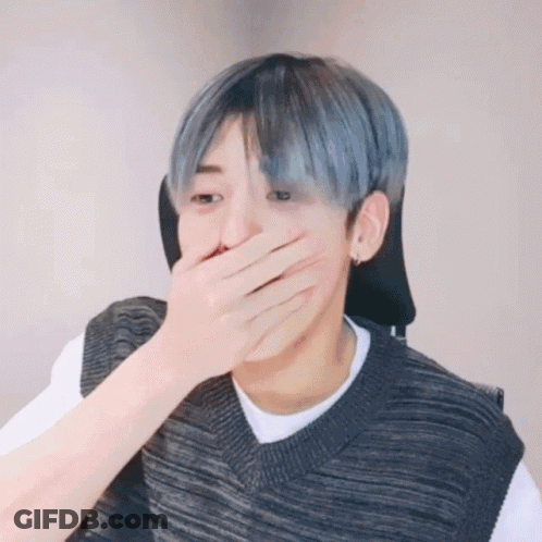 A Man With Blue Hair Is Covering His Mouth With His Hand While Wearing A Sweater Vest . GIF
