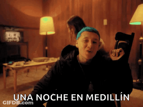 A Man With Blue Hair Is Sitting In A Chair With The Words Una Noche En Medellin Above Him GIF