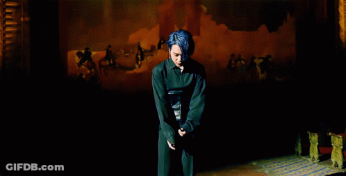 A Man With Blue Hair Stands In Front Of A Painting That Says ' A ' On It GIF