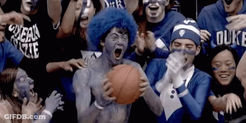 A Man With Blue Paint On His Face Is Holding A Basketball In Front Of A Crowd Of People Wearing Duke Shirts GIF