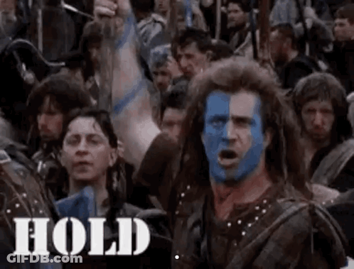 A Man With Blue Paint On His Face Is Standing In Front Of A Crowd Of People With Their Arms In The Air . GIF