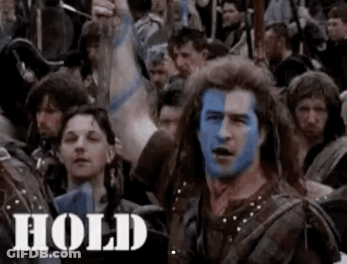 A Man With Blue Paint On His Face Is Surrounded By A Crowd Of People . GIF