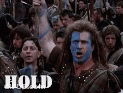 A Man With Blue Paint On His Face Stands In Front Of A Crowd With The Word Hold On The Bottom Right GIF