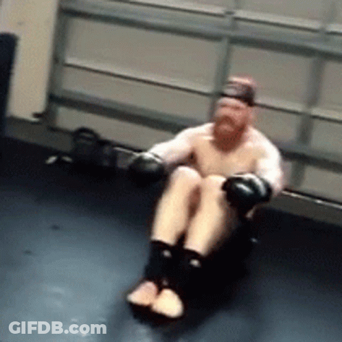 A Man With Boxing Gloves Is Sitting On A Black Mat GIF