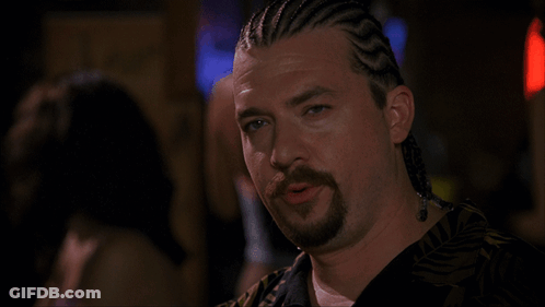 A Man With Braids On His Hair And A Beard Looks At The Camera GIF