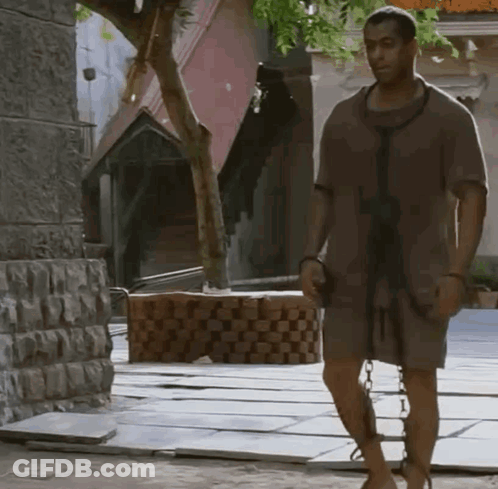 A Man With Chains Around His Legs Is Walking Down A Street GIF
