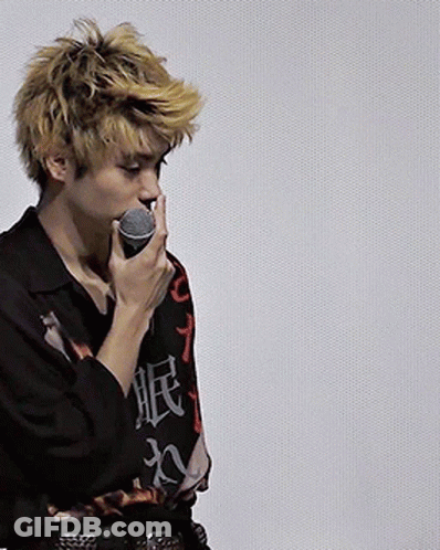 A Man With Chinese Writing On His Shirt Is Holding A Microphone In His Mouth GIF