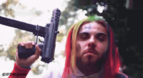 A Man With Colorful Hair Is Holding A Gun In His Right Hand . GIF
