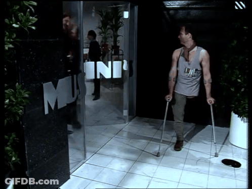 A Man With Crutches Is Walking In Front Of A Building That Says Mini GIF