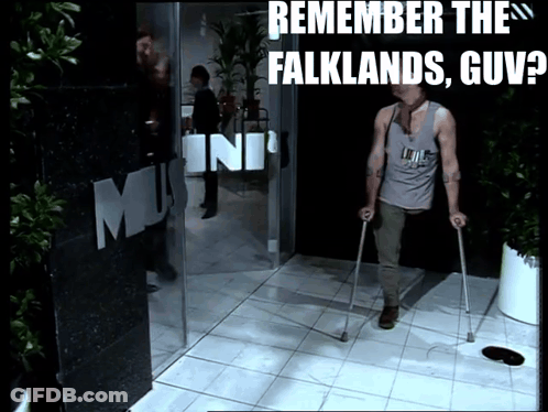 A Man With Crutches Walks In Front Of A Sign That Says Remember The Falklands GIF