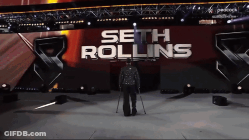 A Man With Crutches Walks On A Stage In Front Of A Sign That Says Seth Rollins GIF