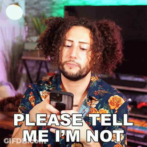 A Man With Curly Hair And A Beard Is Holding A Cell Phone And Says Please Tell Me I 'M Not GIF
