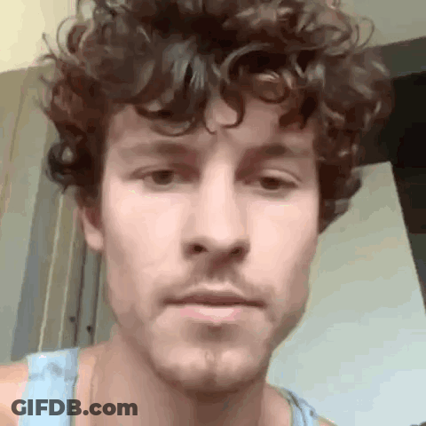 A Man With Curly Hair And A Beard Is Looking At The Camera . GIF