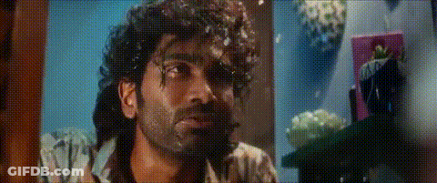A Man With Curly Hair And A Beard Is Looking At The Camera In A Room . GIF