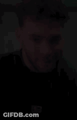 A Man With Curly Hair And A Beard Is Smiling And Wearing A Black T-Shirt . GIF