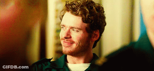 A Man With Curly Hair And A Beard Is Smiling While Standing Next To Another Man . GIF