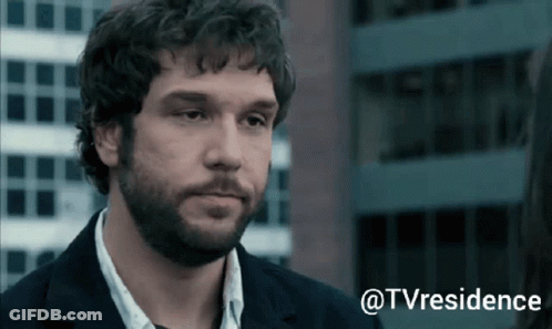 A Man With Curly Hair And A Beard Is Standing In Front Of A Building With The Words @Tvresidence Above Him GIF