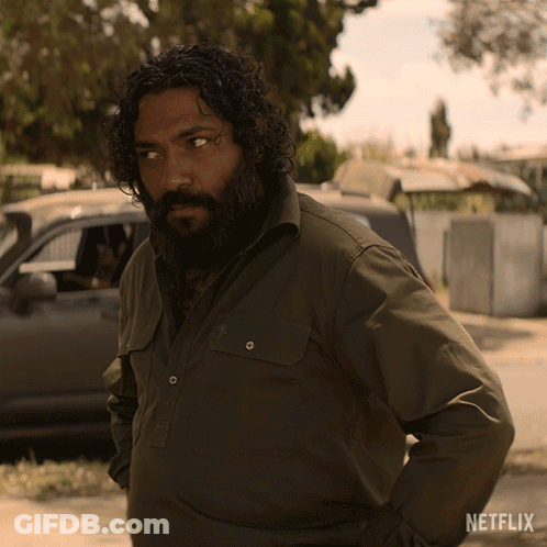 A Man With Curly Hair And A Beard Is Standing In Front Of A Netflix Logo GIF