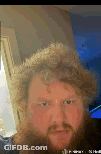 A Man With Curly Hair And A Beard Is Taking A Selfie In A Room GIF