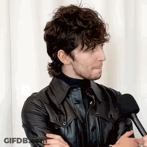 A Man With Curly Hair And A Beard Is Talking Into A Microphone . GIF