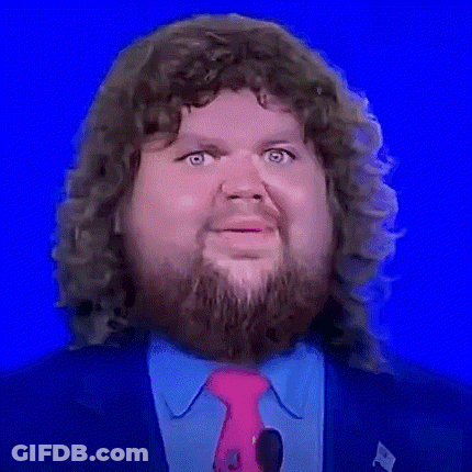A Man With Curly Hair And A Beard Is Wearing A Pink Tie And A Blue Suit . GIF
