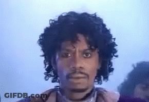 A Man With Curly Hair And A Beard Is Wearing A Purple Jacket . GIF