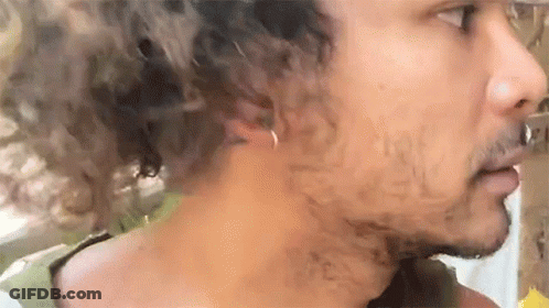 A Man With Curly Hair And A Beard Is Wearing A Ring In His Ear . GIF