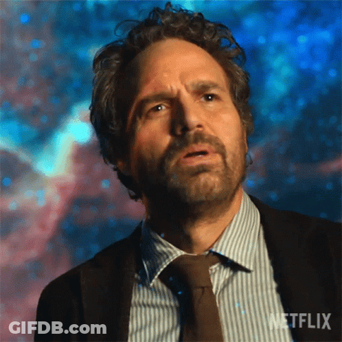 A Man With Curly Hair And A Beard Is Wearing A Suit And Tie And Looking Up At The Sky . GIF