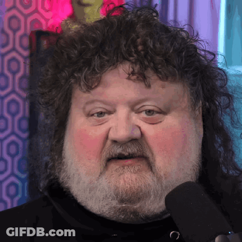 A Man With Curly Hair And A Beard Looks At The Camera GIF