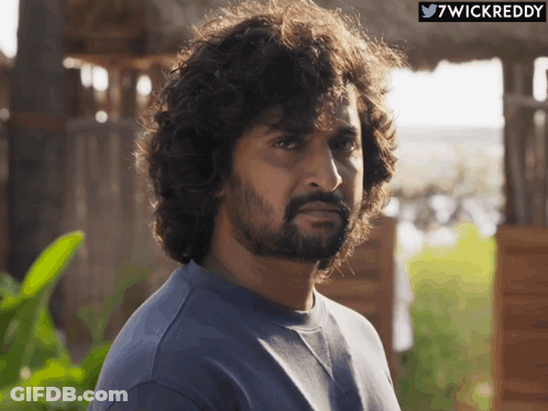 A Man With Curly Hair And A Beard Looks At The Camera With A Twitter Icon Above Him That Says 7Wickreddy GIF
