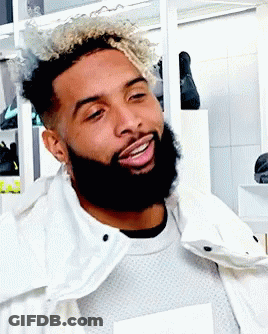 A Man With Curly Hair And A Beard Wearing A White Jacket GIF