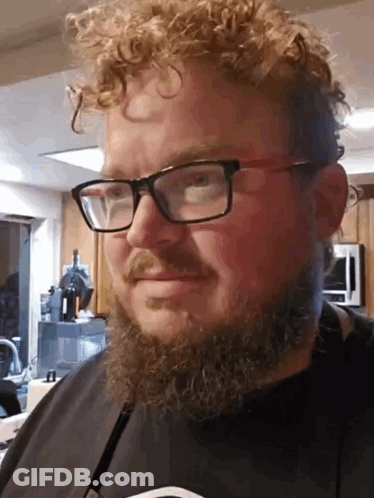 A Man With Curly Hair And A Beard Wearing Glasses And A Black Shirt GIF