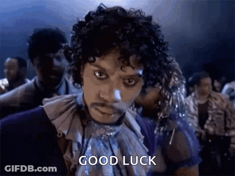A Man With Curly Hair And A Mustache Is Standing In Front Of A Crowd Of People . GIF