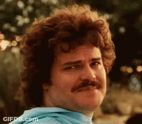 A Man With Curly Hair And A Mustache Is Wearing A Blue Hoodie And Making A Funny Face . GIF