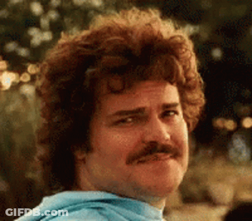A Man With Curly Hair And A Mustache Is Wearing A Blue Sweatshirt And Making A Funny Face . GIF