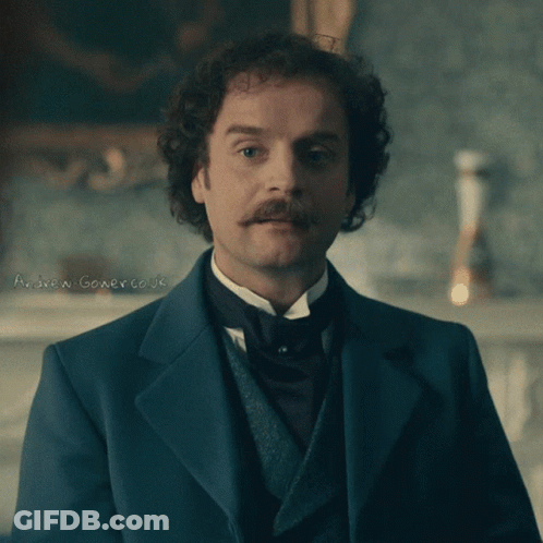 A Man With Curly Hair And A Mustache Is Wearing A Suit And Tie GIF