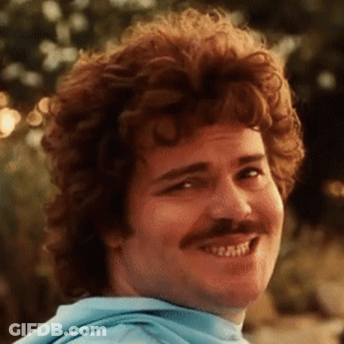 A Man With Curly Hair And A Mustache Smiles GIF