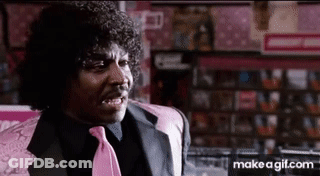 A Man With Curly Hair And A Pink Tie Is Sitting In A Chair In A Store . GIF