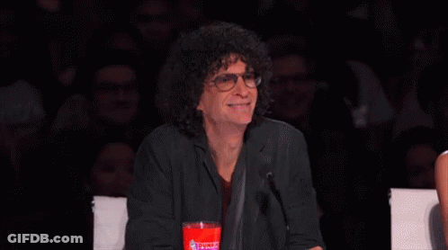 A Man With Curly Hair And Glasses Is Sitting In Front Of A Microphone Holding A Cup Of Coca Cola . GIF