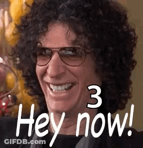 A Man With Curly Hair And Glasses Is Smiling And Saying Hey Now . GIF