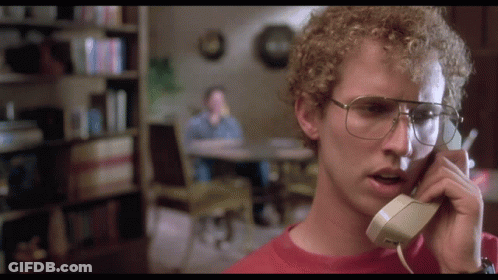 A Man With Curly Hair And Glasses Is Talking On A Phone GIF
