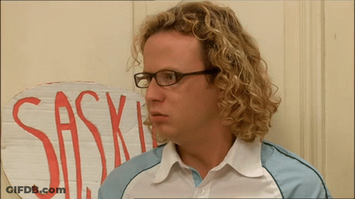 A Man With Curly Hair And Glasses Stands In Front Of A Sign That Says Sas GIF