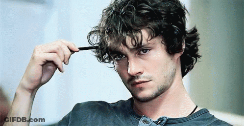 A Man With Curly Hair Is Brushing His Hair With A Comb And Looking At The Camera . GIF
