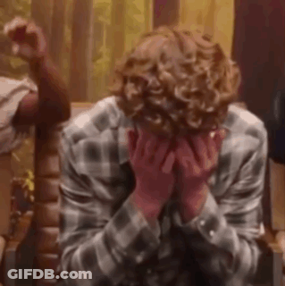 A Man With Curly Hair Is Covering His Face With His Hands While Sitting On A Chair . GIF